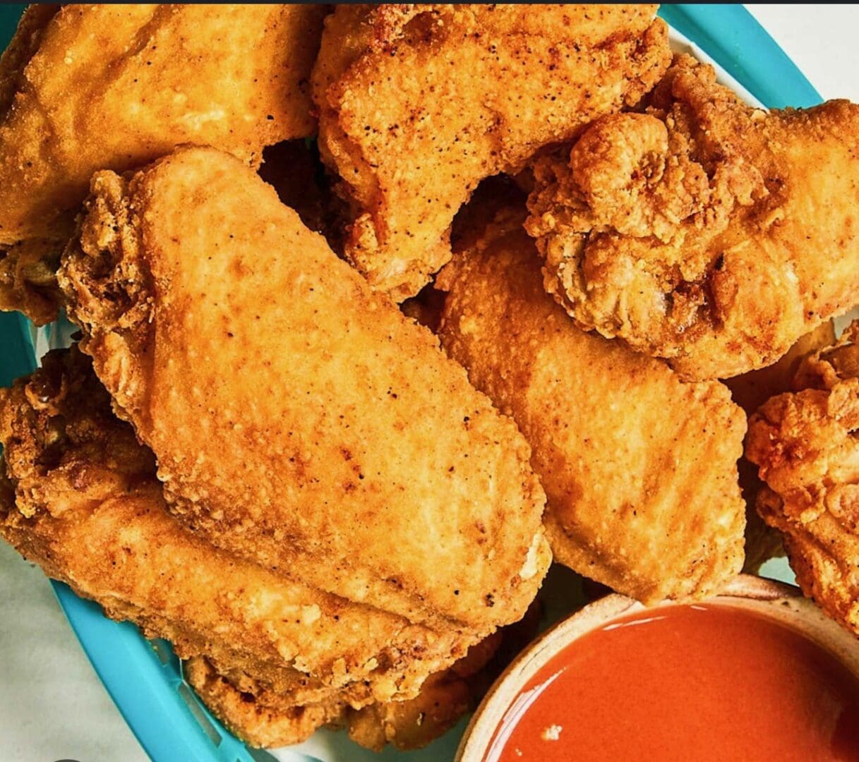 Crispy fried chicken wings with a side of dipping sauce.